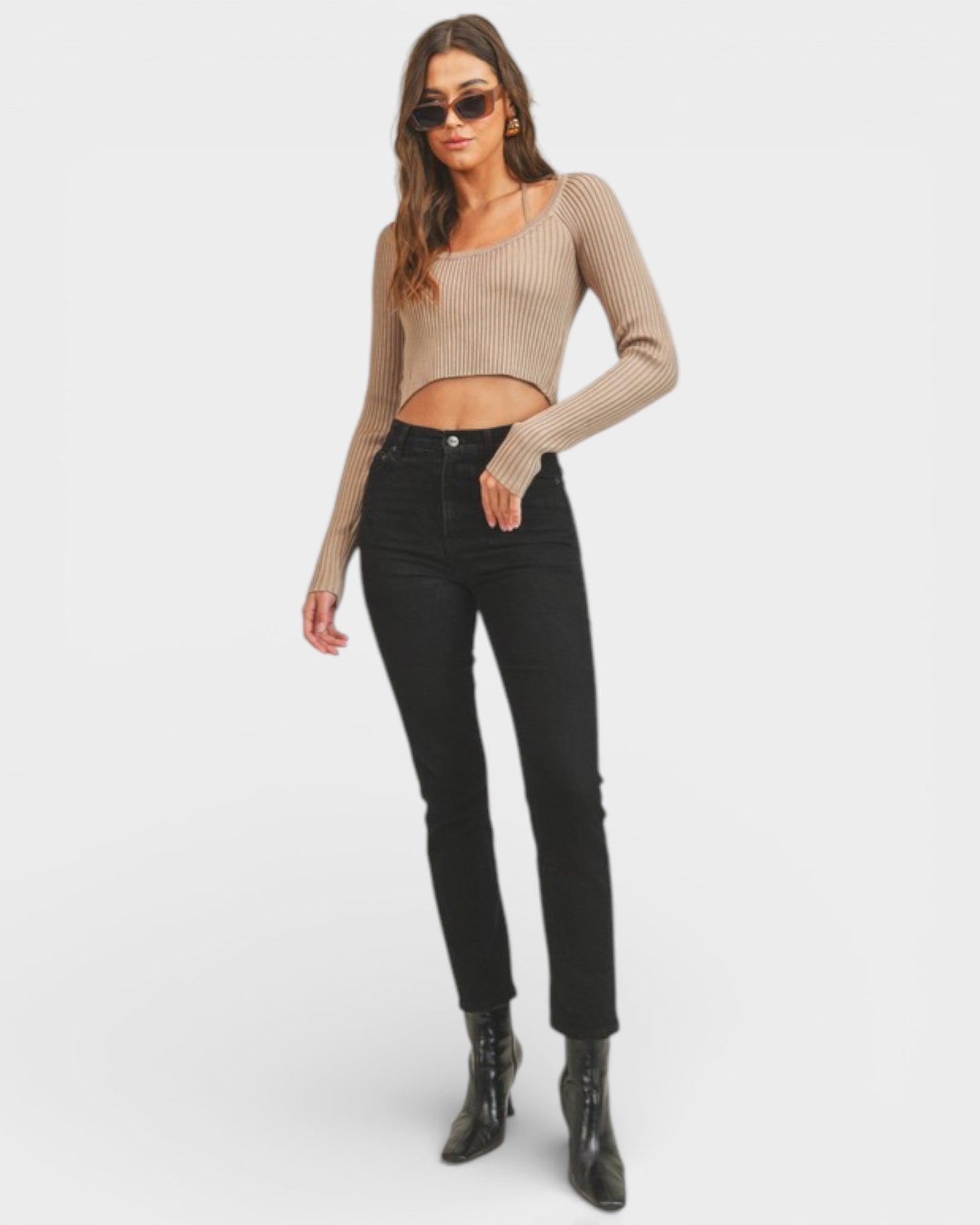 Woman wearing a beige long-sleeve top and black jeans on a white background