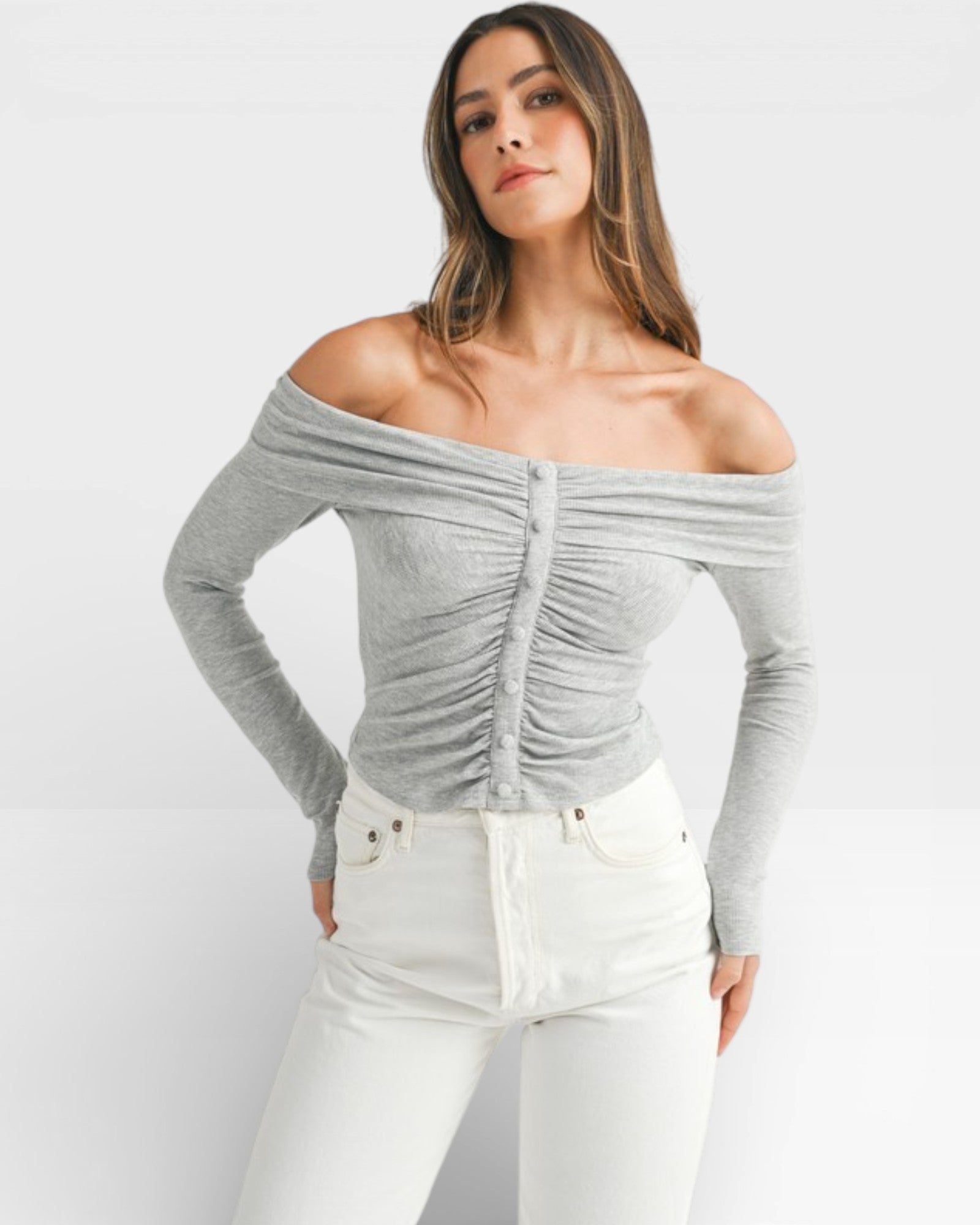 Woman wearing a gray off-shoulder top and white pants on a light gray background