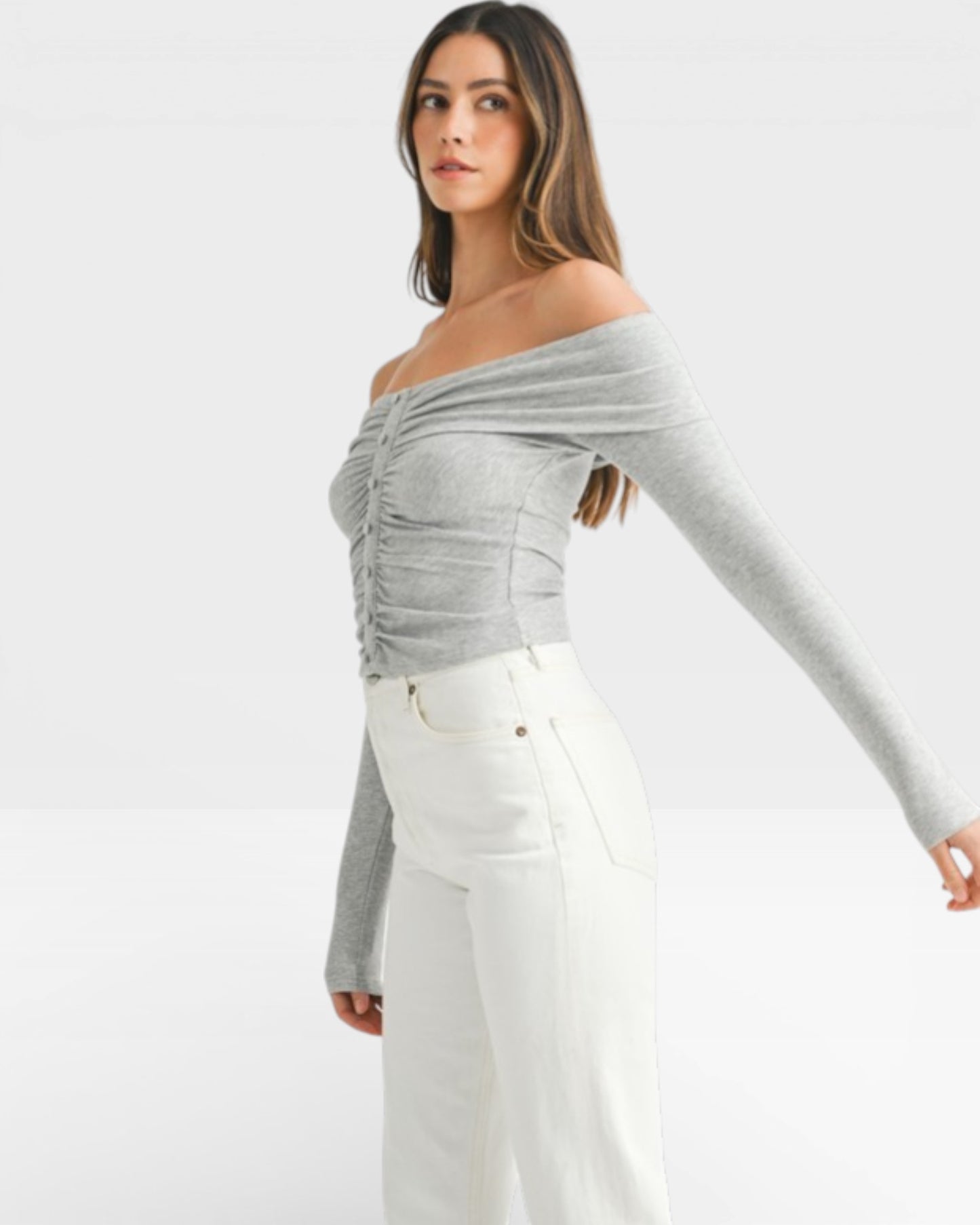 Woman wearing a gray off-shoulder top and white pants on a white background