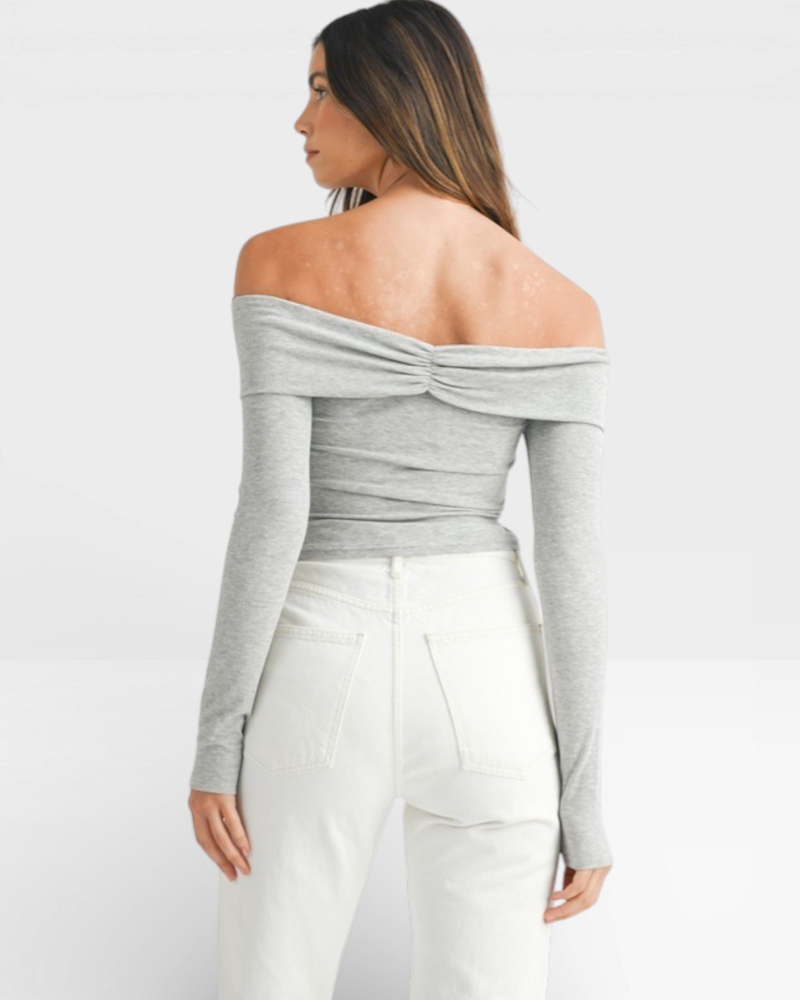 Woman wearing a gray off-shoulder top and white pants on a white background