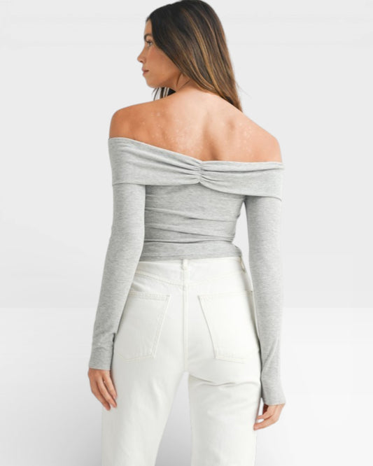 Woman wearing a gray off-shoulder top and white pants on a white background