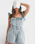 Woman wearing a denim romper and white cap on a white background