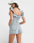 Woman wearing a light blue denim dress with ruffled straps on a white background