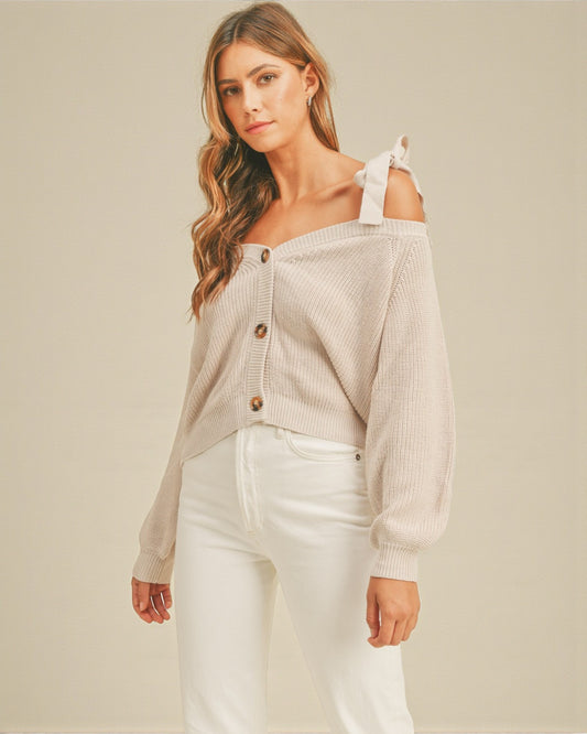 Woman wearing a beige off-shoulder cardigan with white pants on a beige background