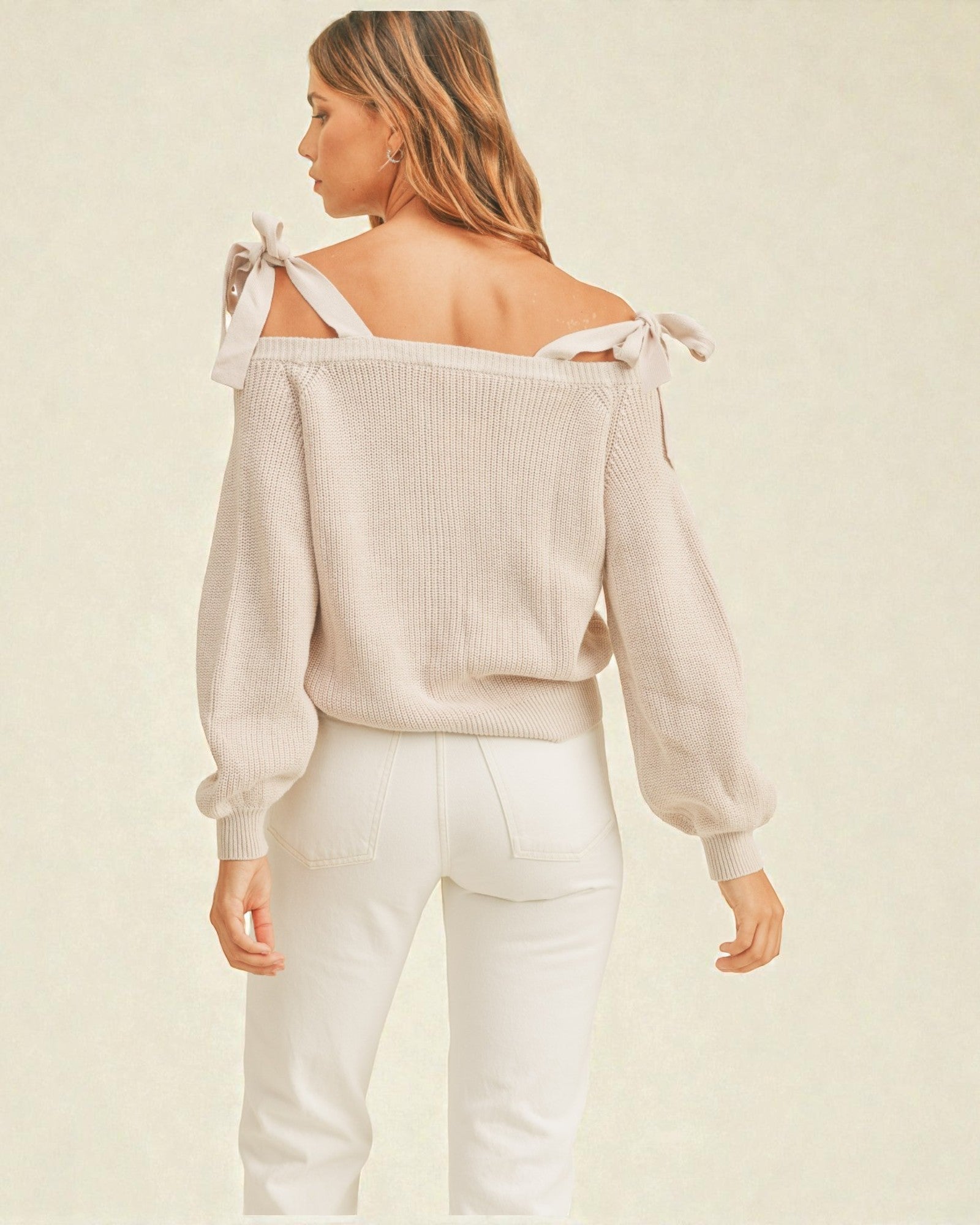 Woman wearing a beige off-shoulder top with white pants on a beige background
