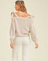 Woman wearing a beige off-shoulder top with white pants on a beige background