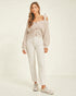 Woman wearing a beige off-shoulder sweater and white pants on a plain background