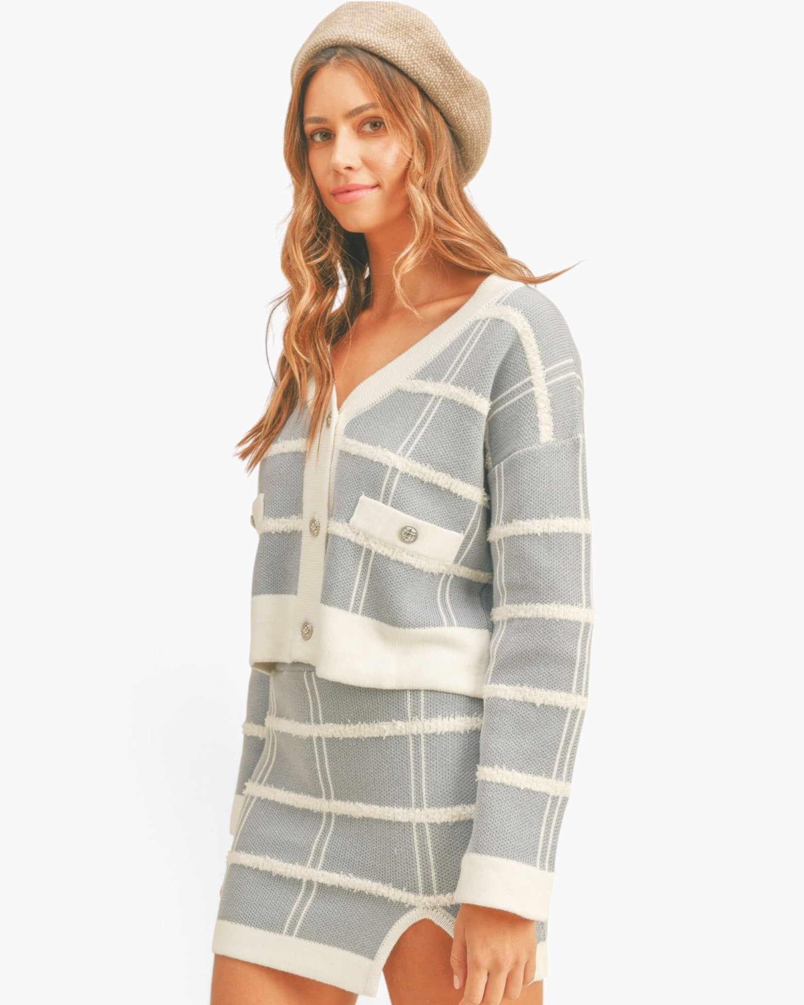 A woman modeling a light gray and cream striped knit cardigan and matching mini skirt set, paired with a beige beret, against a plain white studio background.