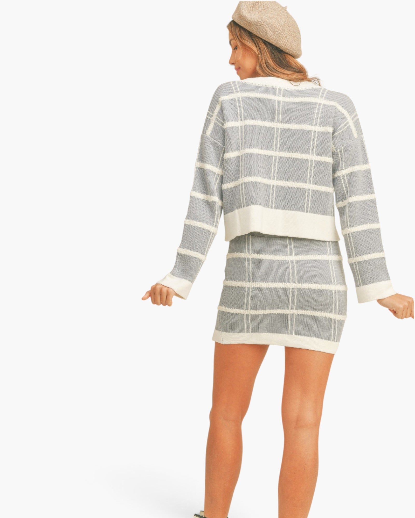 A woman shown from the back wearing a gray and white plaid knit sweater and matching mini skirt, with a beige beret, against a plain white studio background.
