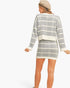 A woman shown from the back wearing a gray and white plaid knit sweater and matching mini skirt, with a beige beret, against a plain white studio background.
