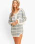 A woman modeling a gray and off-white plaid cardigan dress with a V-neck, button closure, and front pockets, paired with a beige beret, against a plain white studio background.
