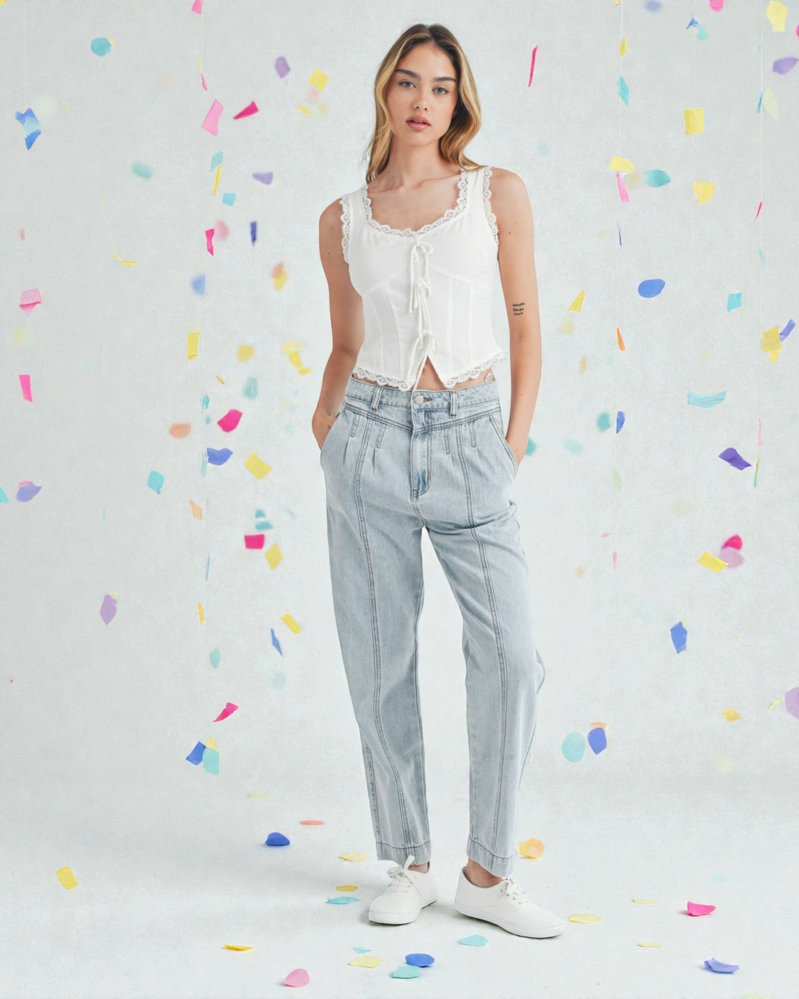 Woman wearing a white sleeveless top and light blue jeans against a colorful confetti background
