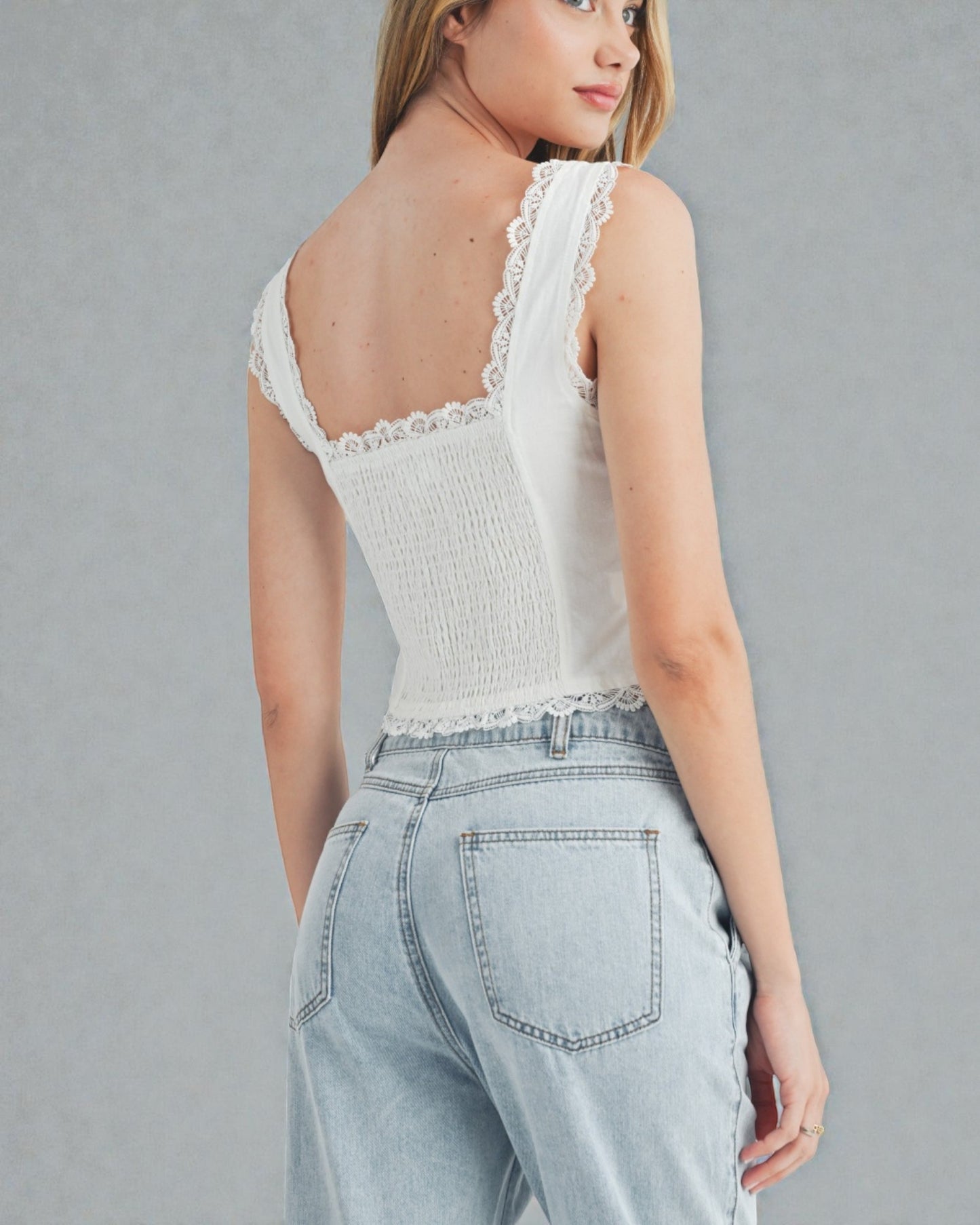 Woman wearing a white lace top and light blue jeans against a gray background