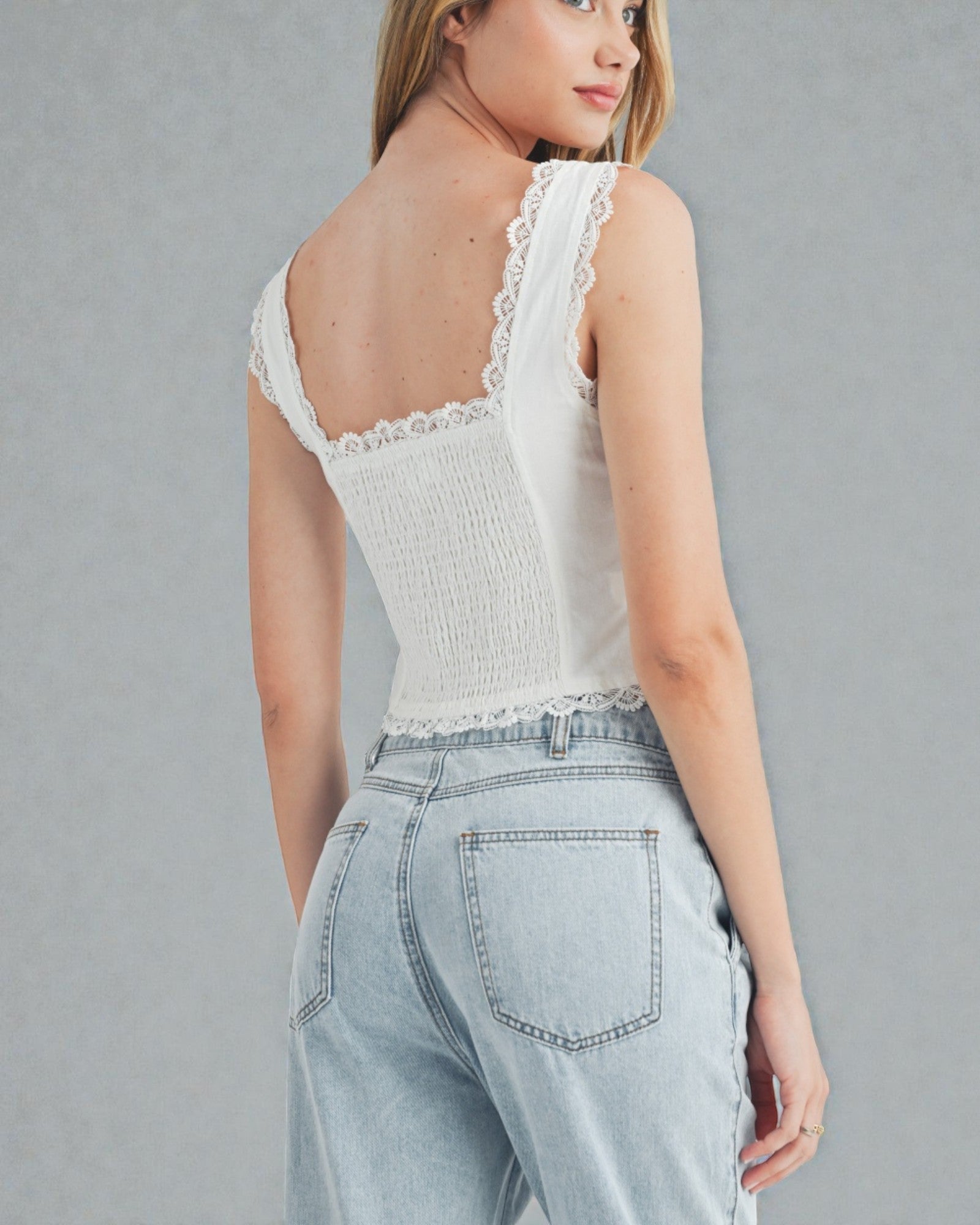 Woman wearing a white lace top and light blue jeans against a gray background