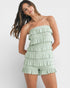 Woman wearing a light green strapless ruffled romper on a white background