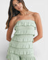 Woman wearing a light green strapless ruffled jumpsuit on a white background