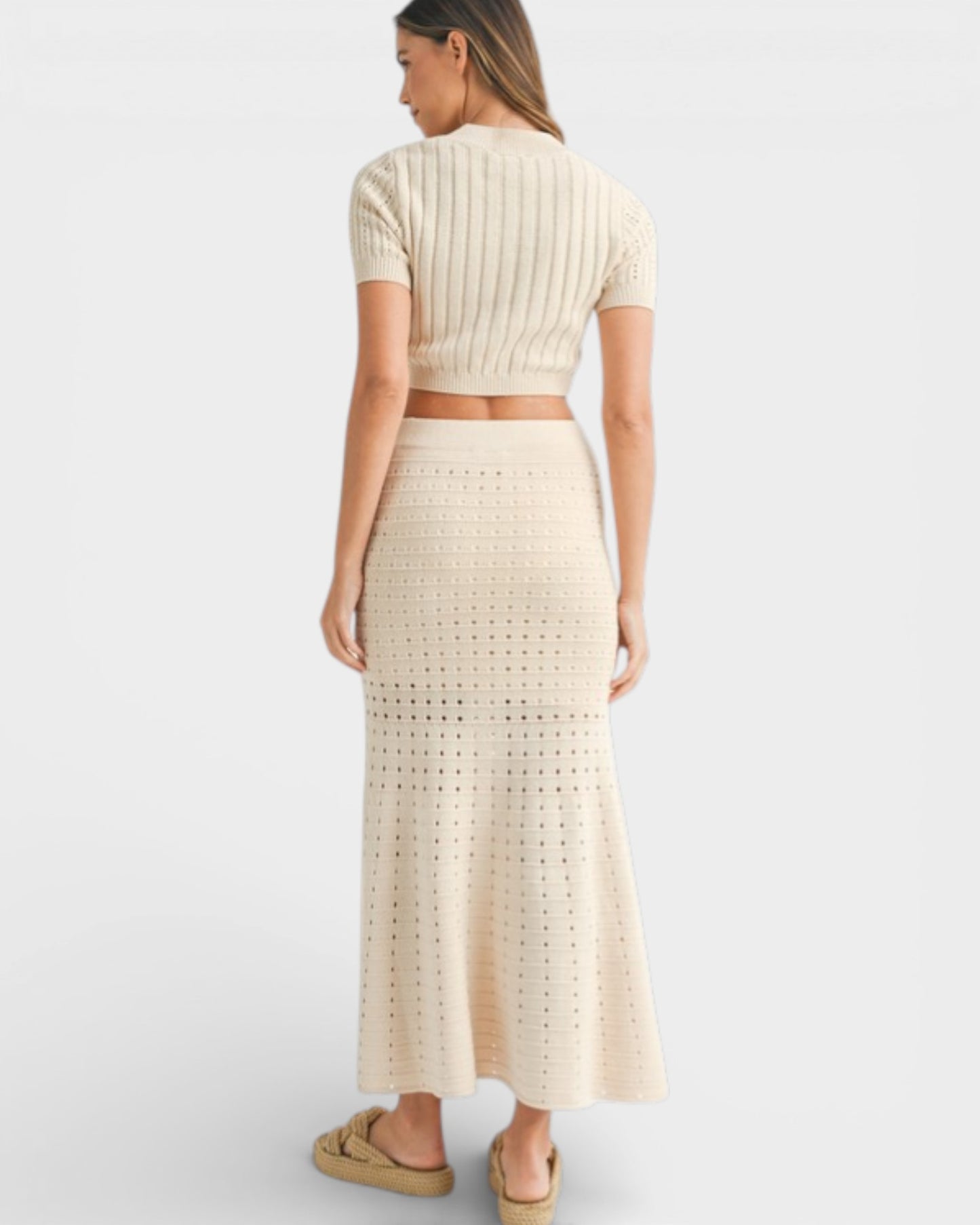 Woman wearing a beige knit top and long skirt on a white background