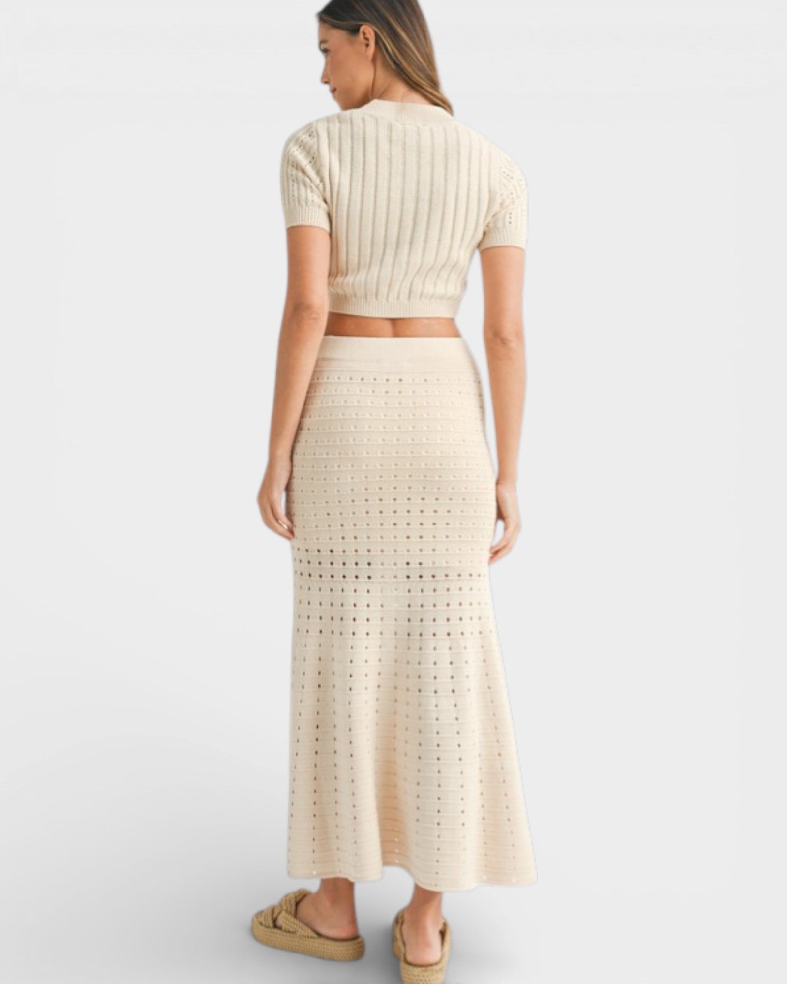 Woman wearing a beige knit top and long skirt on a white background