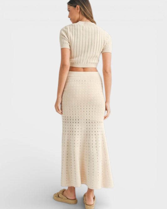 Woman wearing a beige knit top and long skirt on a white background