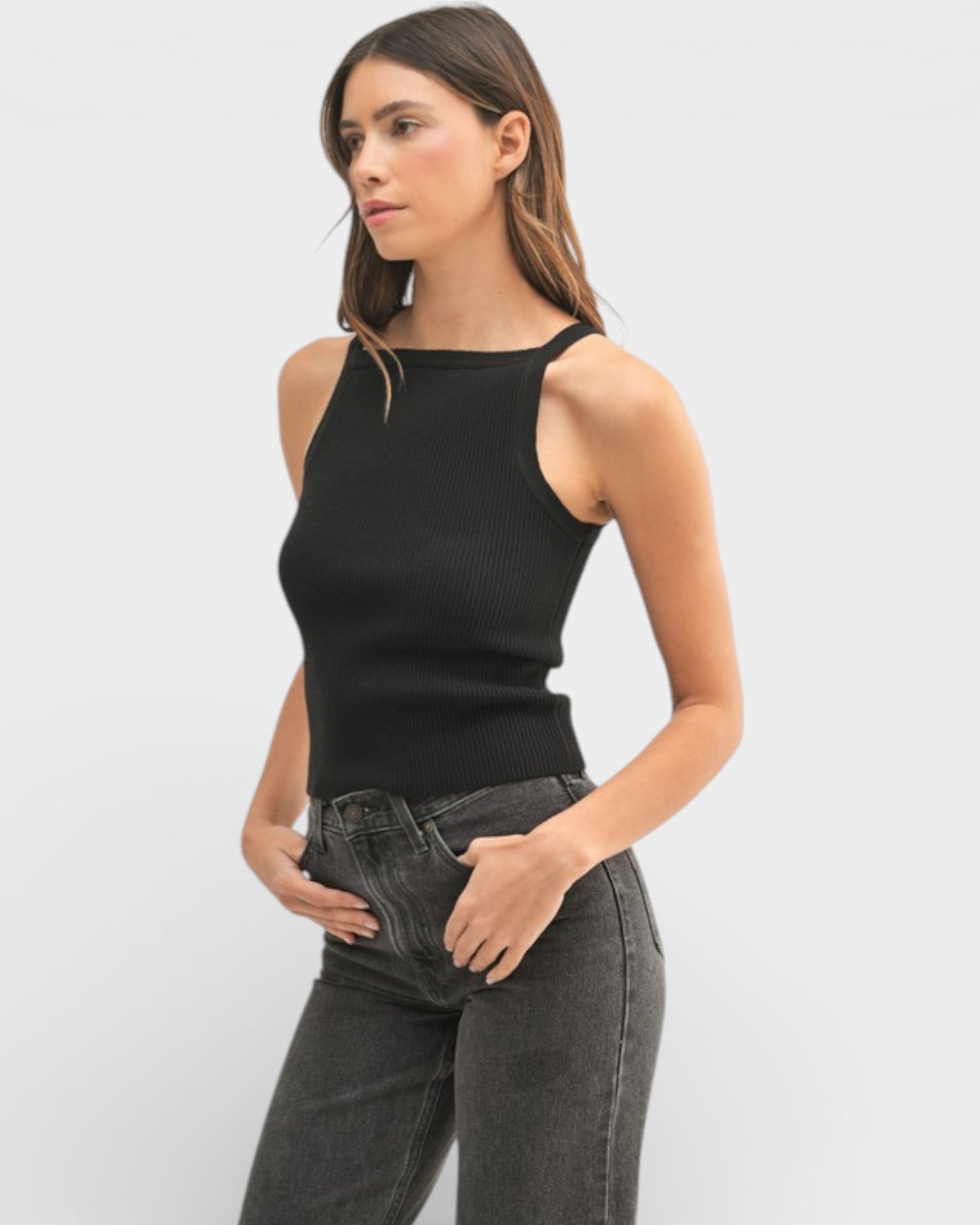 Woman wearing a black sleeveless top and gray jeans on a light gray background