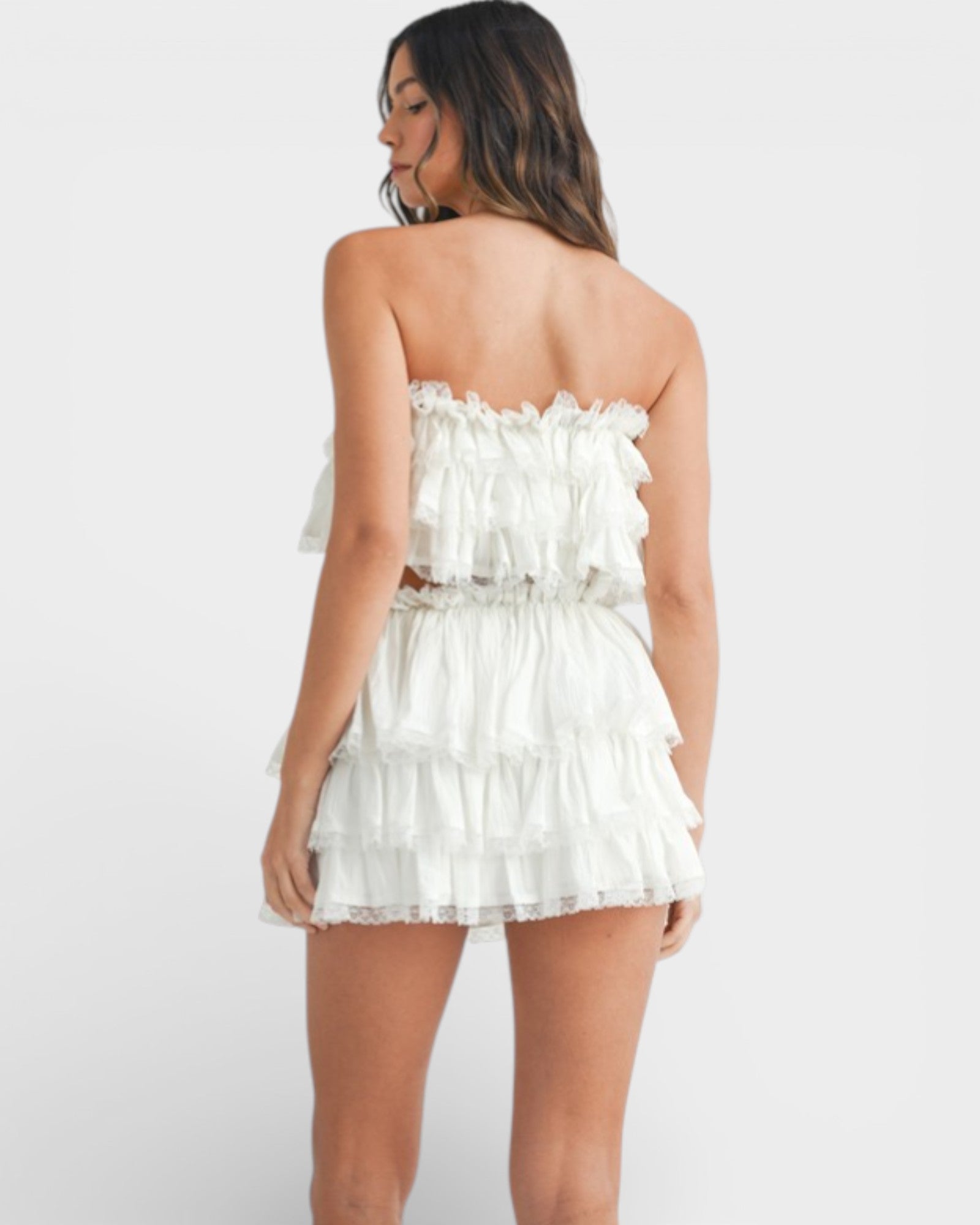 Woman wearing a white strapless dress with ruffled details on a plain background