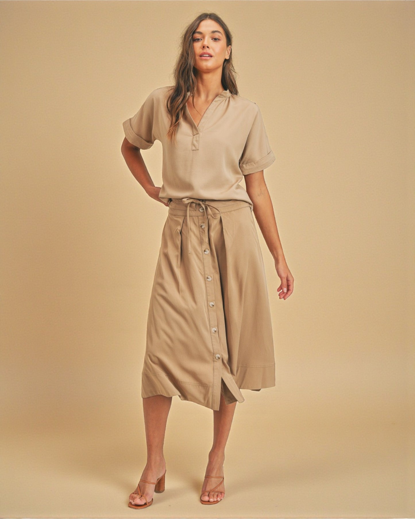 Woman wearing a beige outfit with a shirt and skirt on a beige background