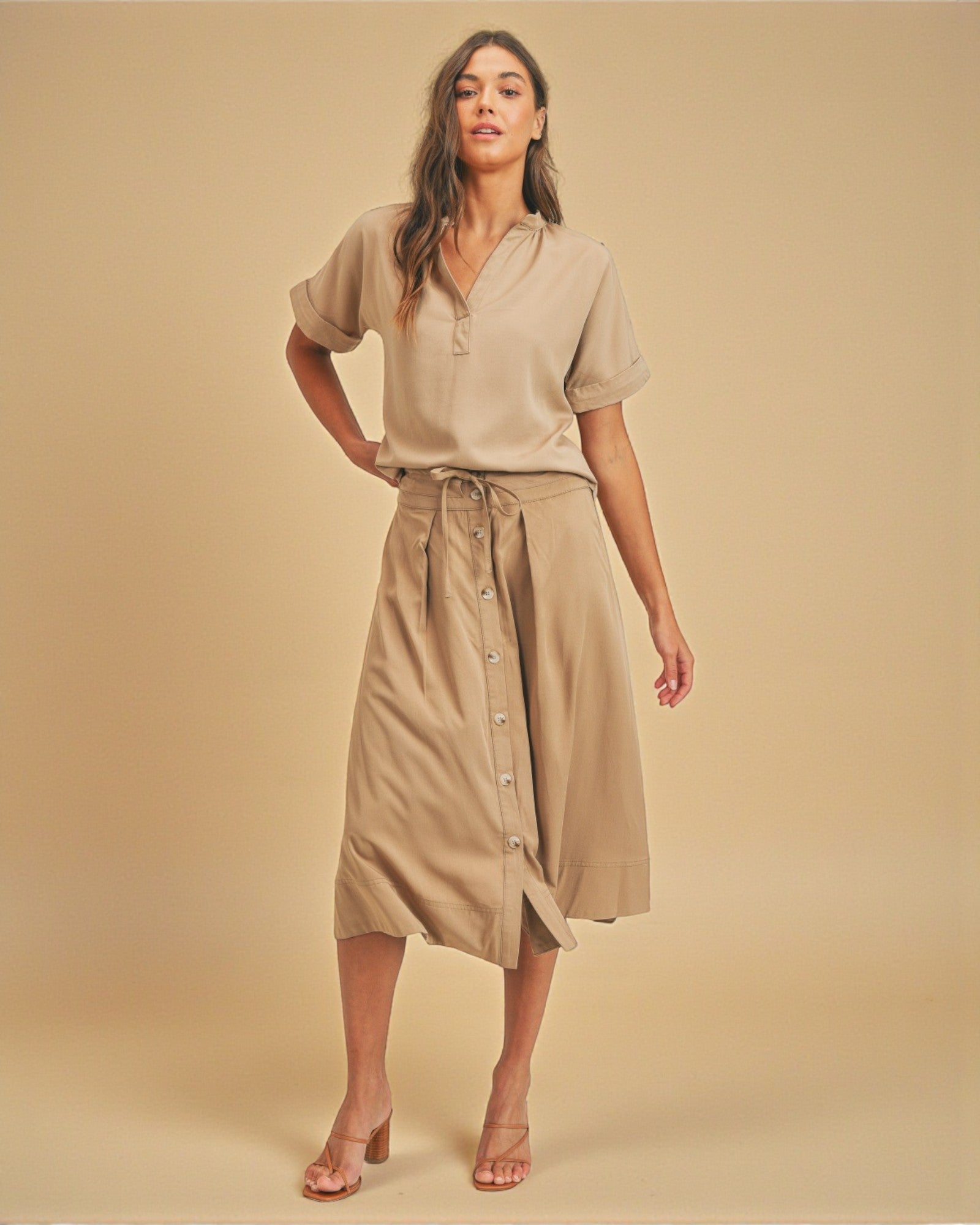 Woman wearing a beige outfit with a shirt and skirt on a beige background