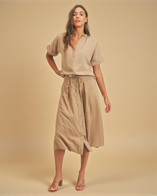 Woman wearing a beige outfit with a shirt and skirt on a beige background