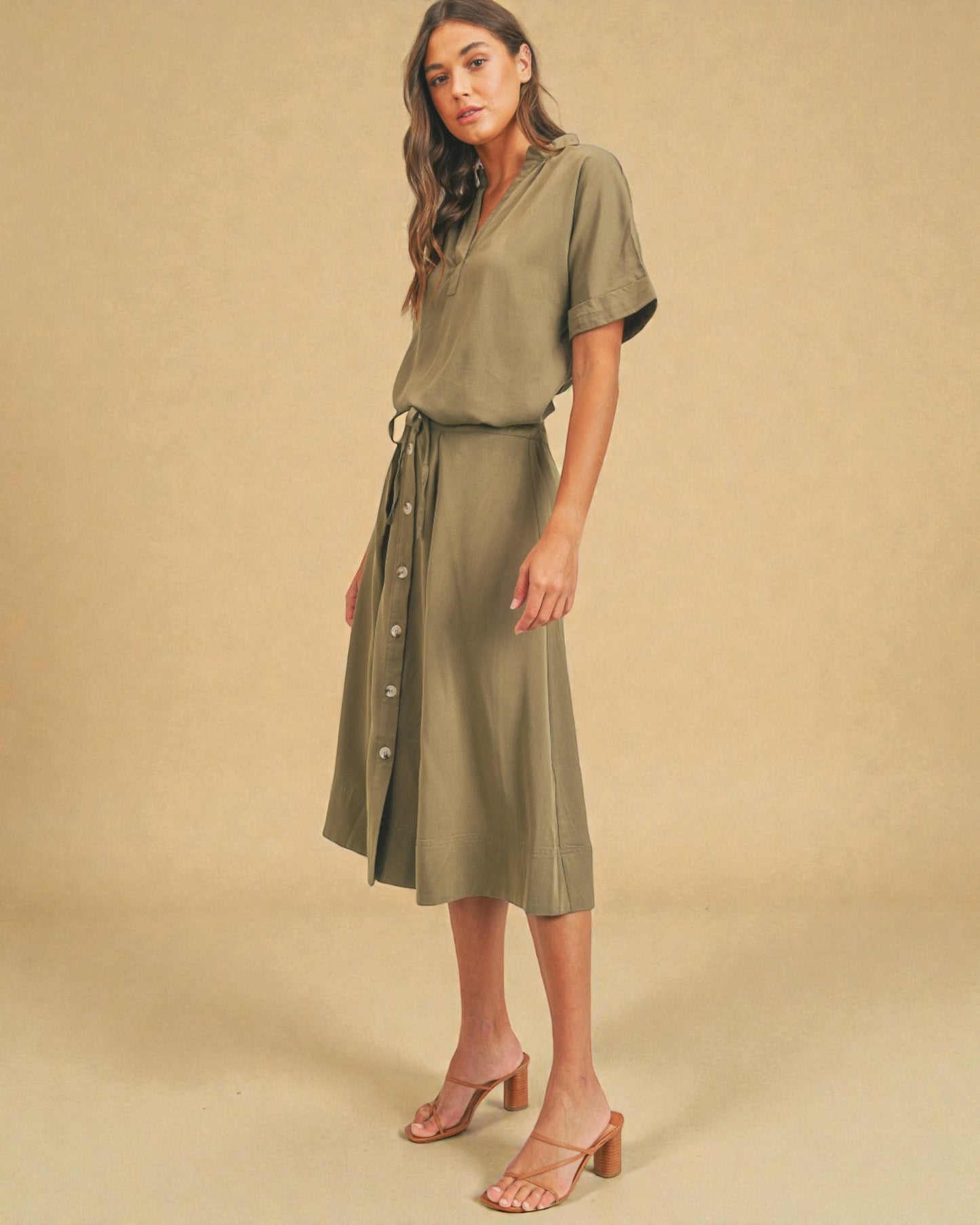 Woman wearing a green dress with a belt against a beige background