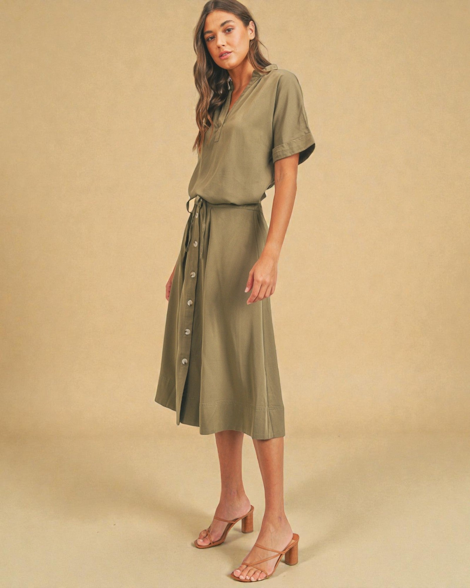 Woman wearing a green dress with a belt against a beige background