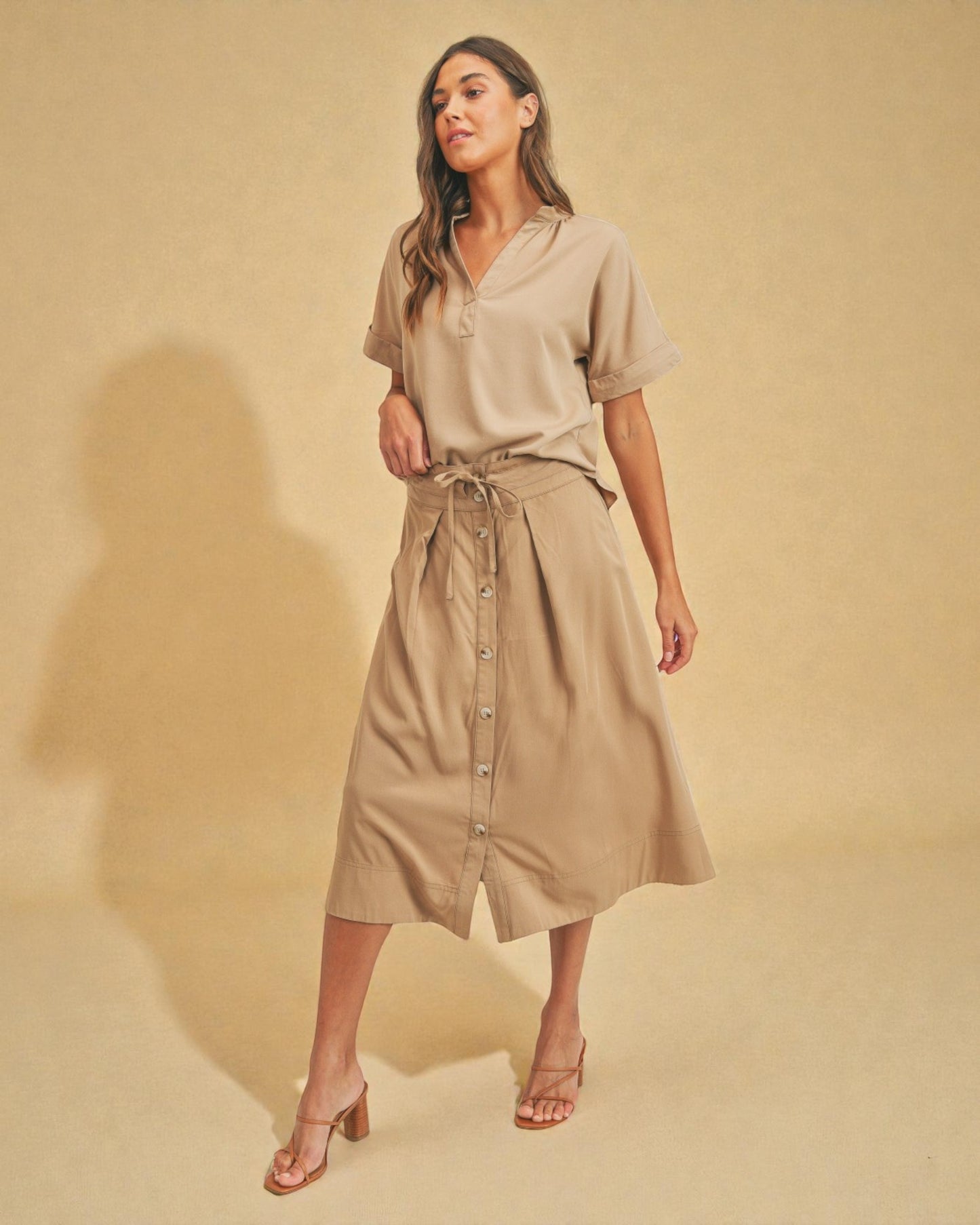 Woman wearing a beige outfit with a skirt and top on a beige background