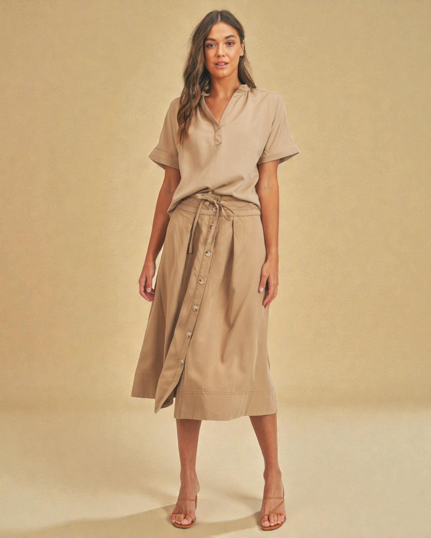 Woman wearing a beige dress with a belt against a beige background