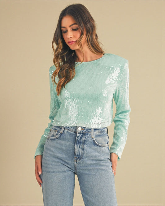 Woman wearing a light blue sequin top and jeans against a beige background