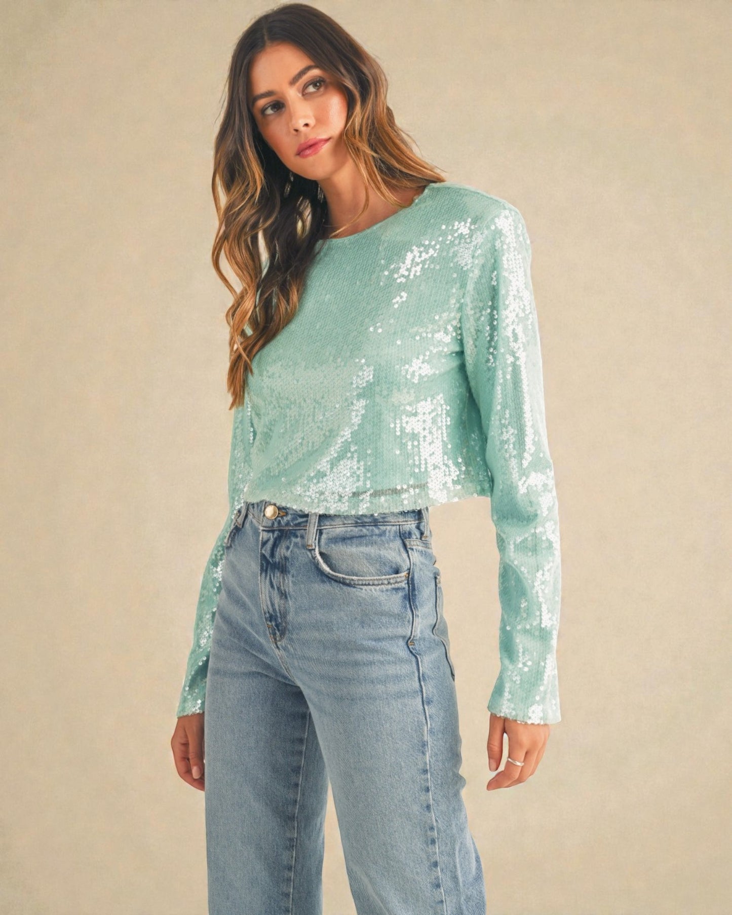 Woman wearing a light blue sequin top and jeans against a beige background