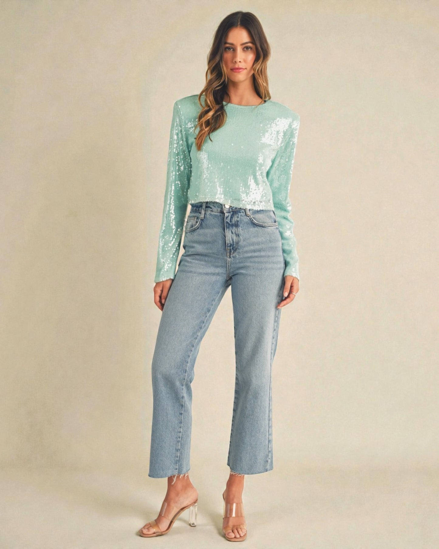 Woman wearing a light blue sequin top and jeans on a beige background