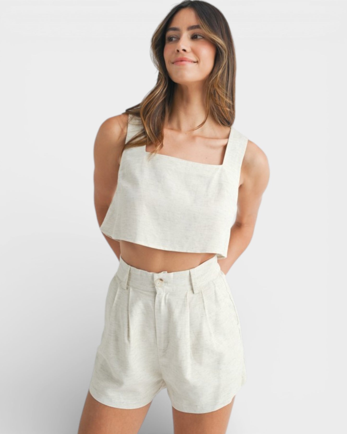 Woman wearing a white sleeveless top and shorts on a plain background