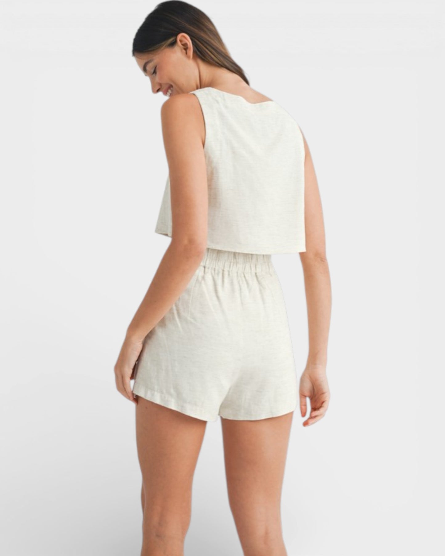 Woman wearing a white sleeveless top and shorts on a plain background