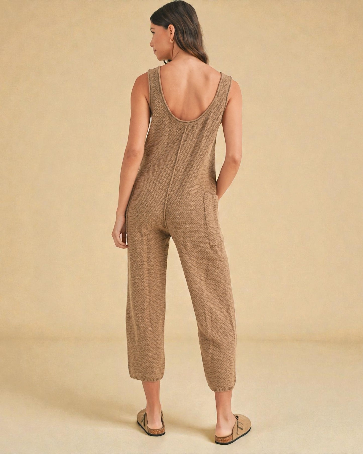 Woman wearing a brown knitted jumpsuit against a beige background