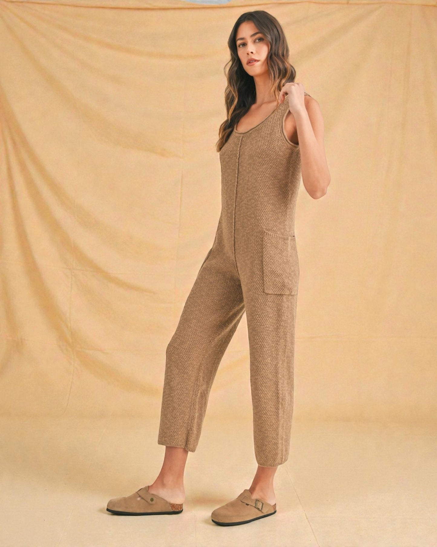 Woman wearing a brown jumpsuit against a beige background