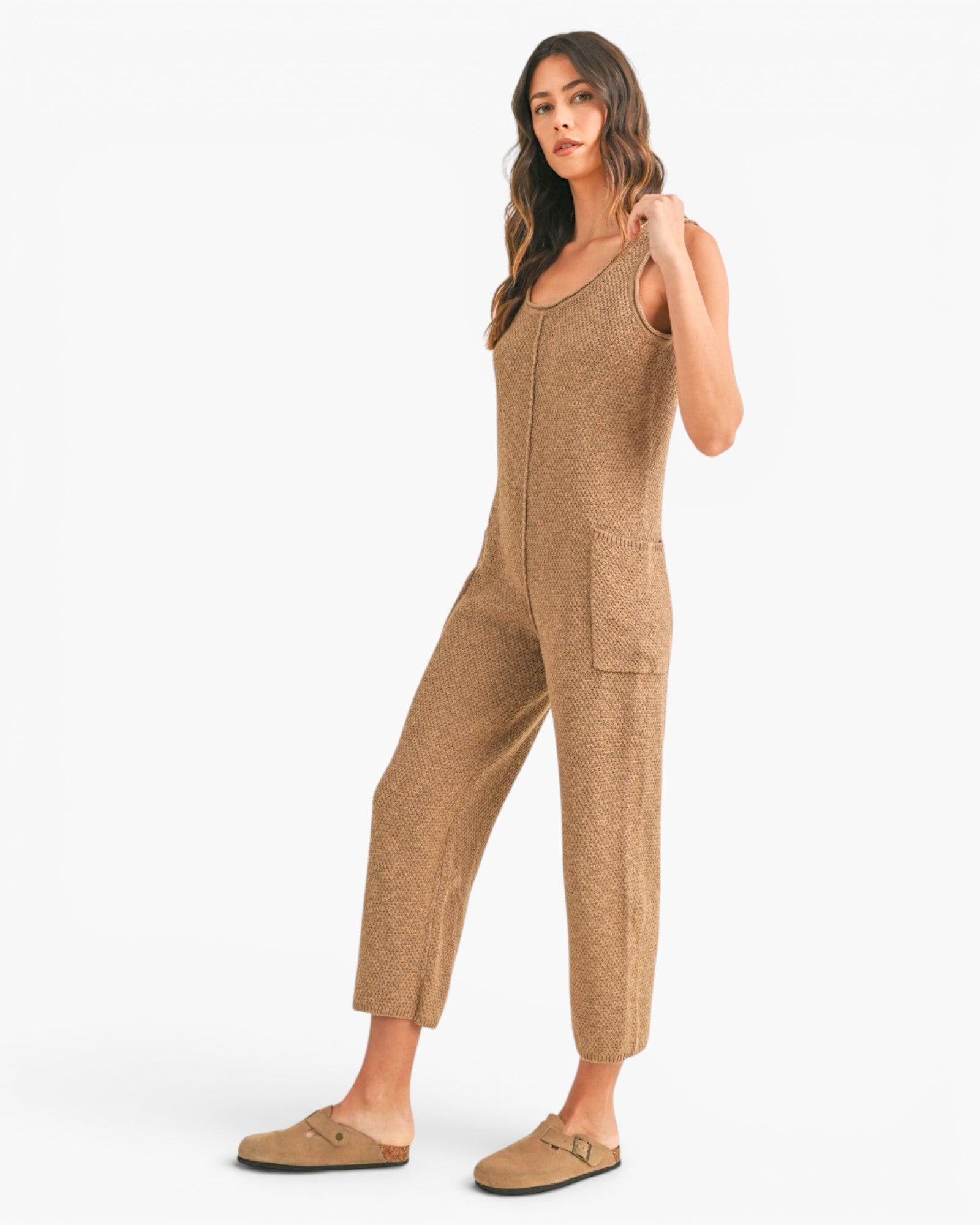 A woman modeling a sleeveless, cropped knit jumpsuit in a heathered tan-brown color, paired with matching tan slip-on shoes, against a plain white studio background.