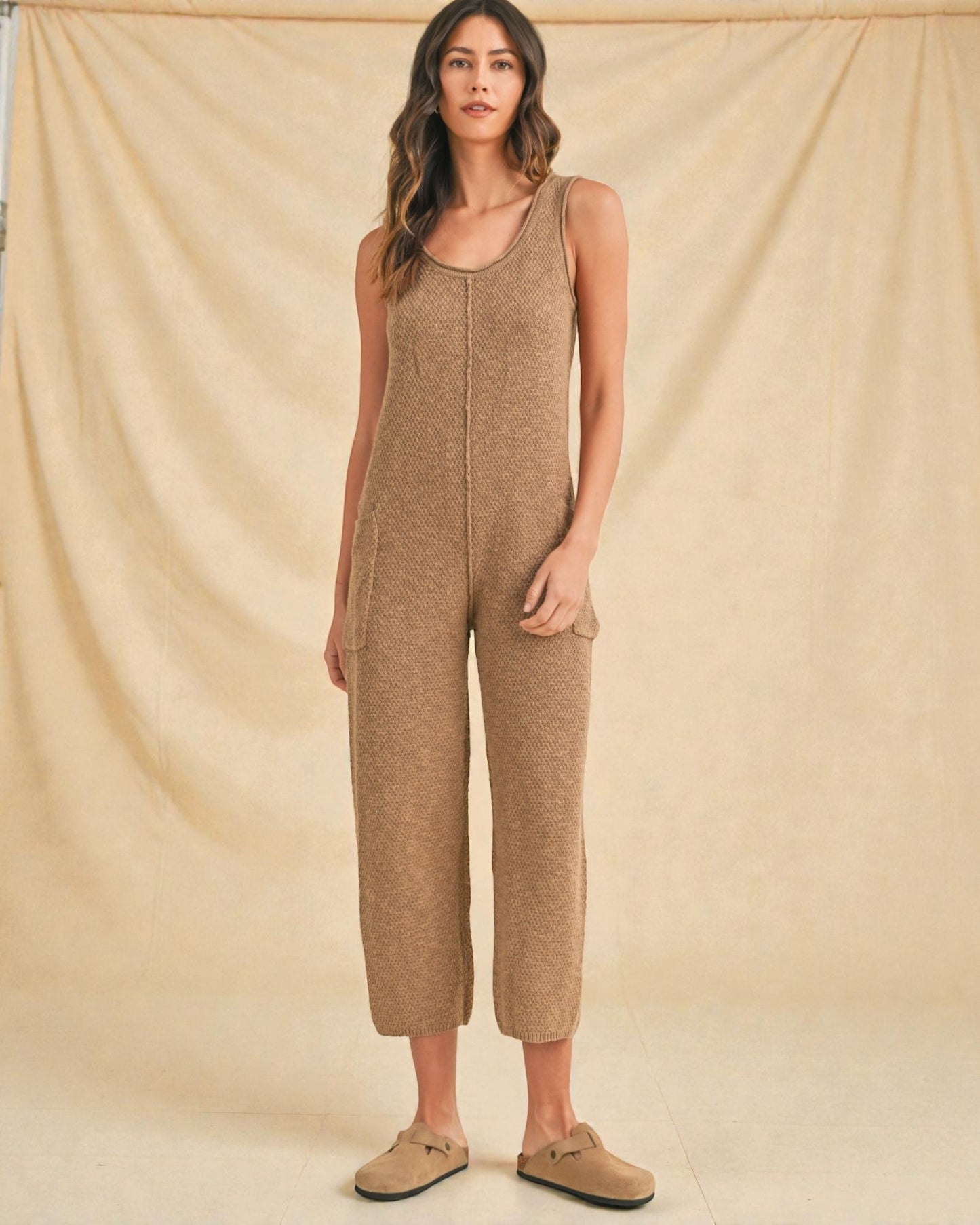 Woman wearing a beige knitted jumpsuit against a beige background