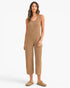 A woman modeling a sleeveless, cropped jumpsuit in a heathered tan color, paired with matching tan slip-on shoes, against a plain white studio background.
