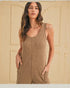 Woman wearing a brown knitted sleeveless jumpsuit against a beige wall.