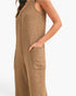 A close-up side view of a woman wearing a textured knit sleeveless jumpsuit in a warm camel brown color, with a side pocket and a visible front zipper.