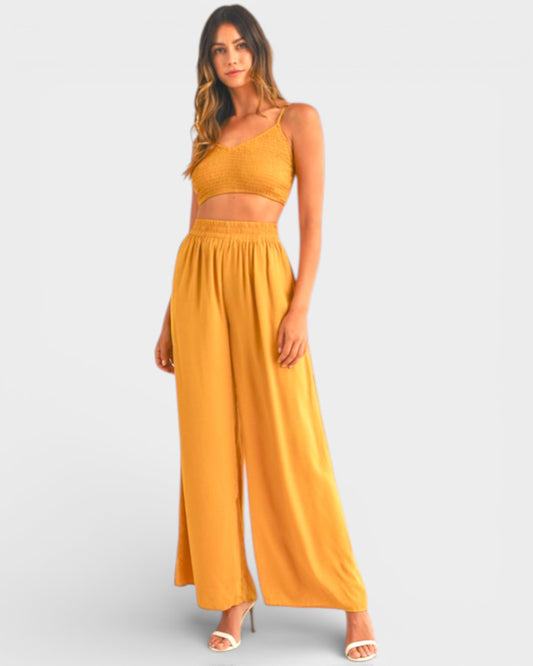 Woman wearing a mustard yellow one-shoulder top and wide-leg pants on a light gray background