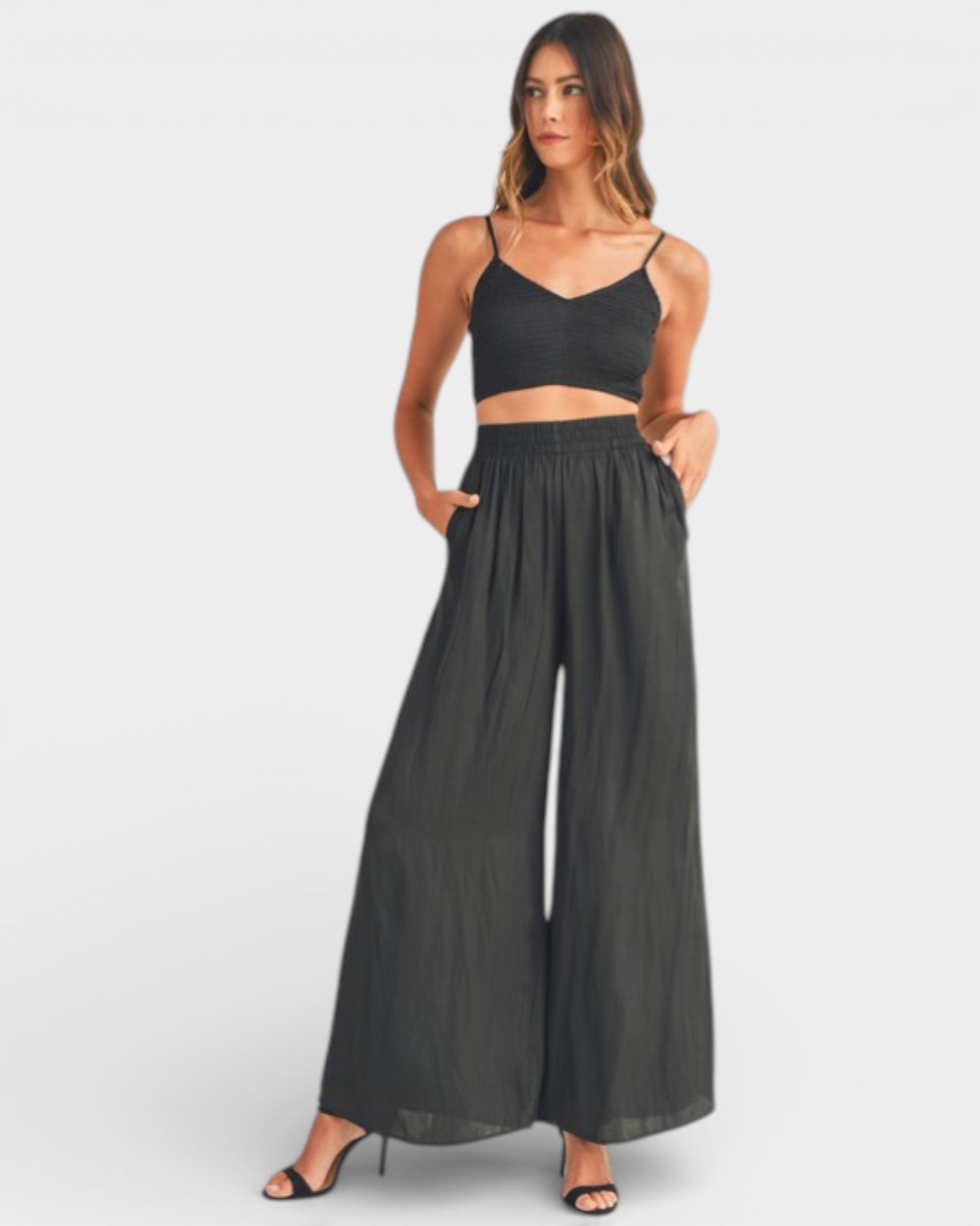 Woman wearing a black crop top and wide-leg pants on a white background
