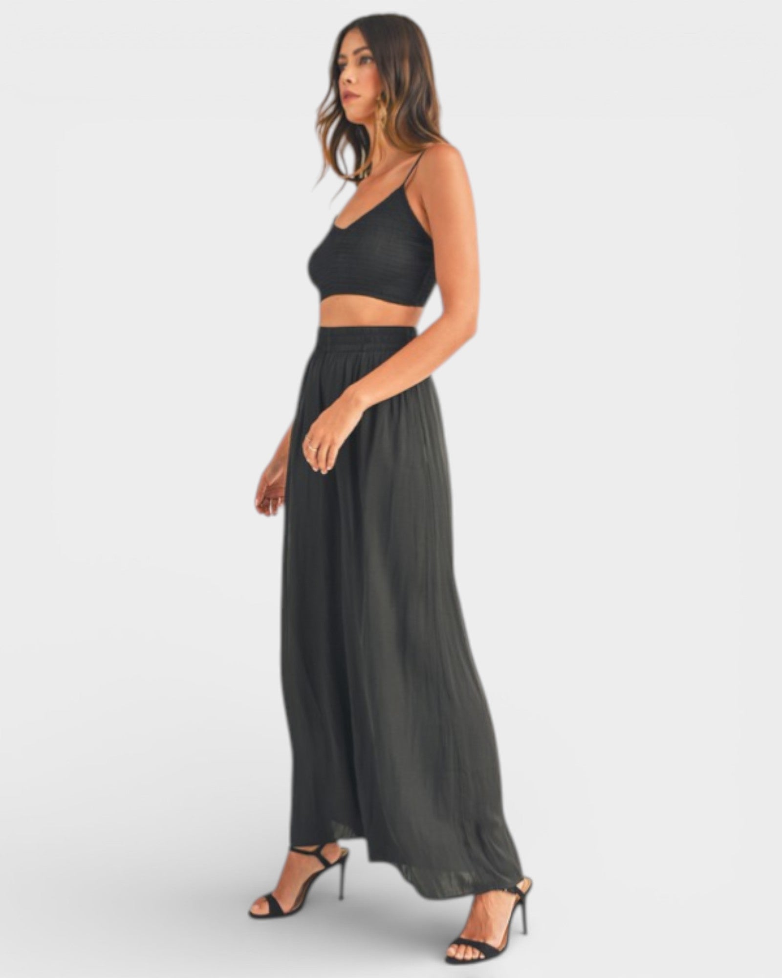 Woman wearing a black crop top and long black skirt on a white background