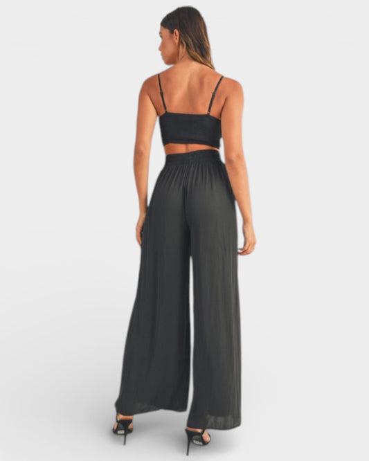 Woman wearing a black strappy top and wide-leg pants on a white background