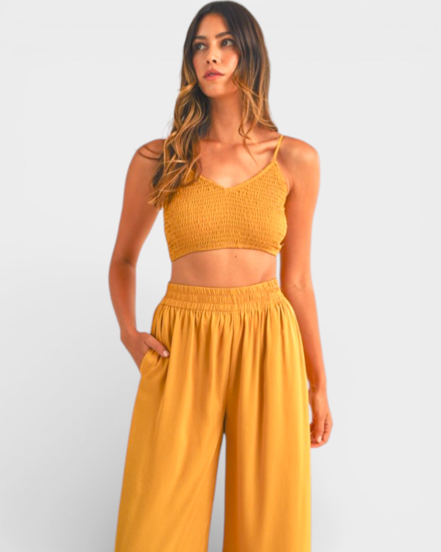 Woman wearing a mustard yellow top and wide-leg pants on a light gray background