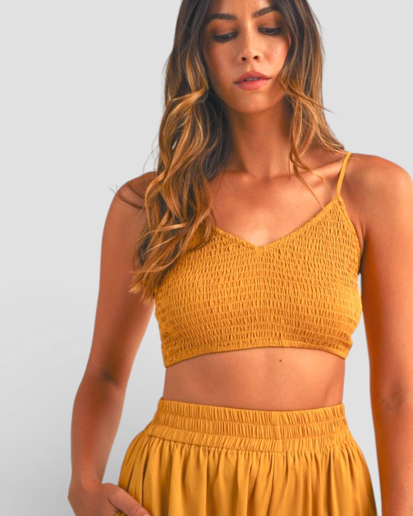 Woman wearing a mustard yellow smocked top and shorts on a light gray background